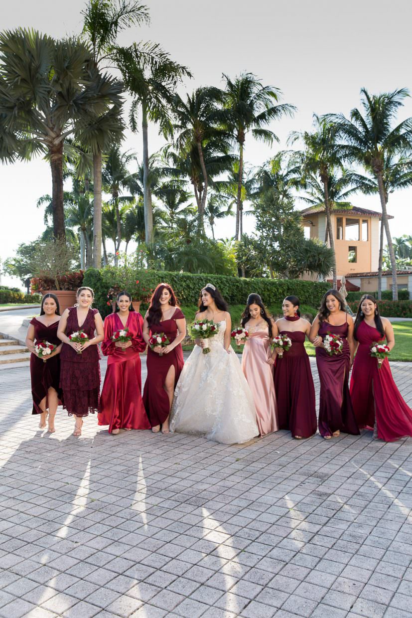Bridesmaids, wearing crimson wedding gowns, walk with a bride during a wedding ceremony at the Biltmore hotel.